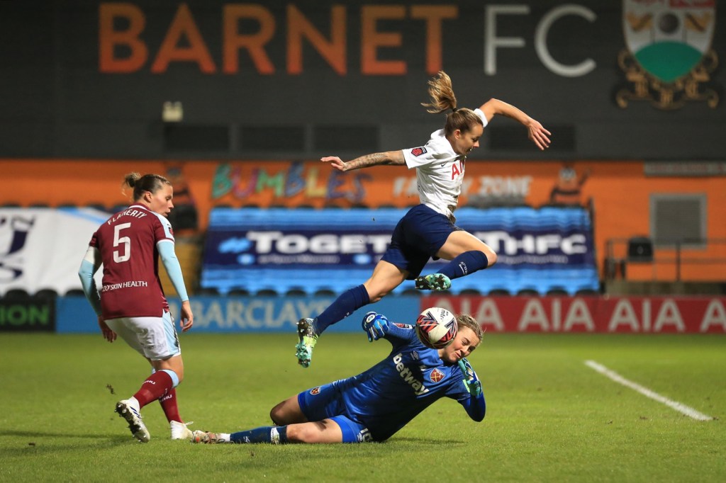 Ria leaping over the goalkeeper as they contest the ball. 